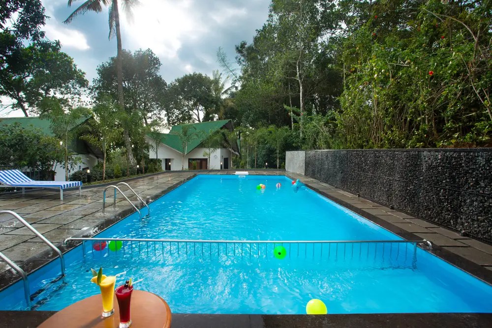 Scenic swimming pool at Misty Lake Resort, Munnar surrounded by lush greenery and misty hills
