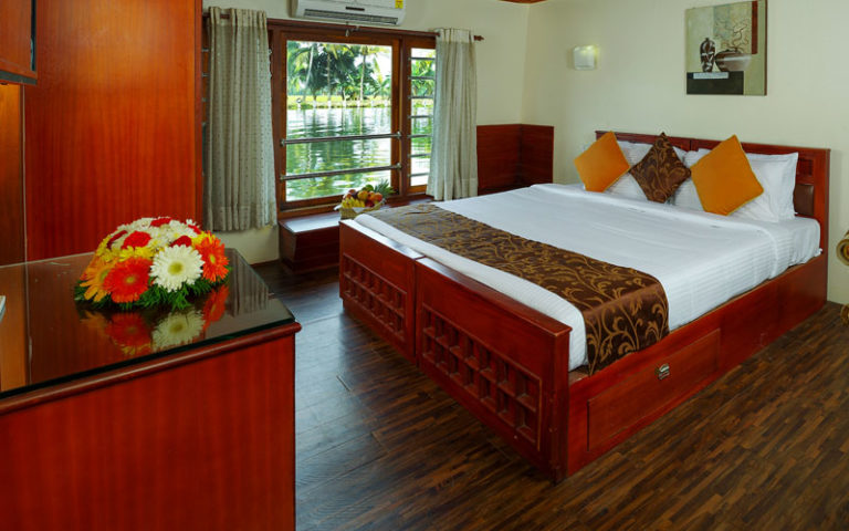 Neatly arranged canal-view bedroom in a family houseboat in Alleppey featuring elegant wooden interiors, soft lighting, and peaceful backwater views.