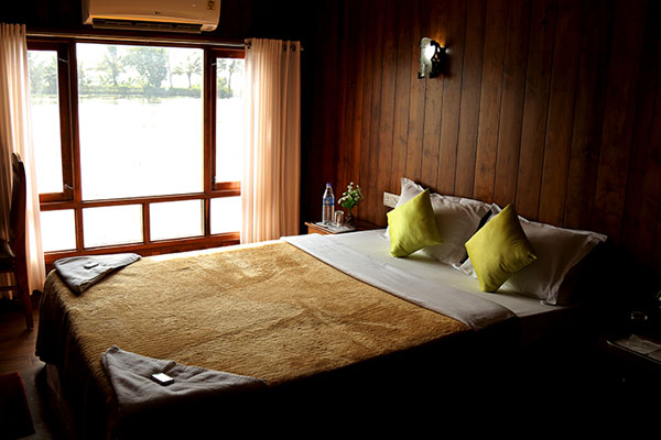 Cozy bedroom in a Kerala houseboat with open windows overlooking the serene backwaters