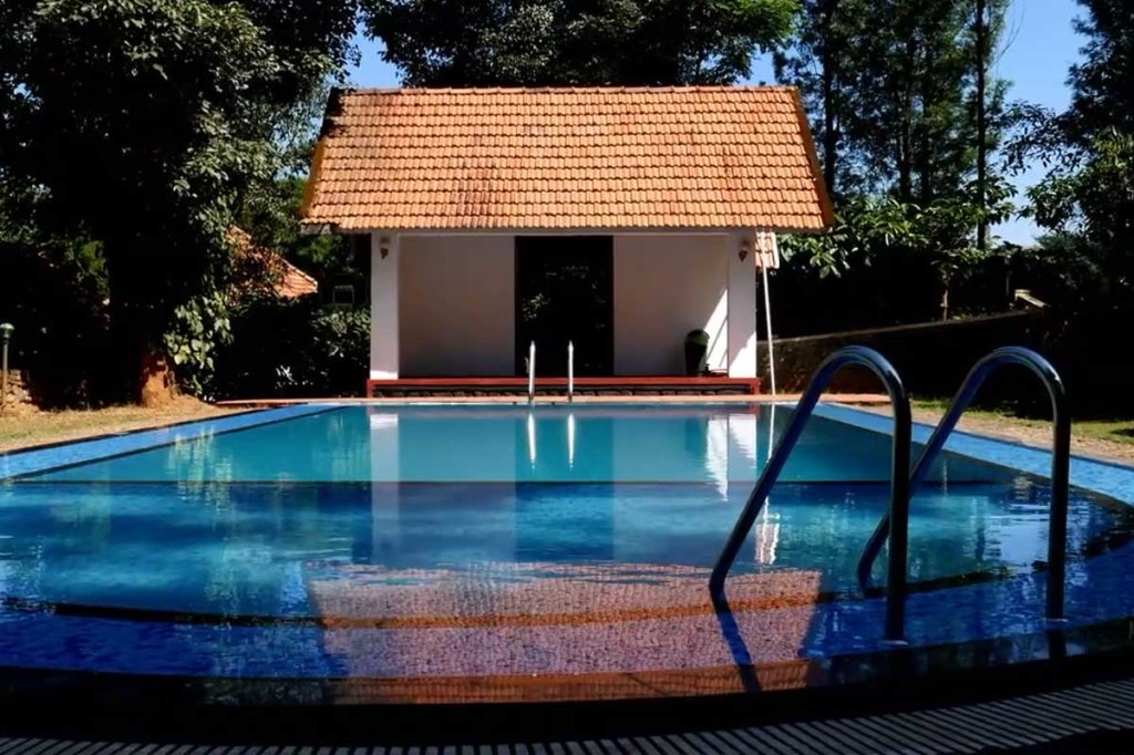 Open-air swimming pool at Misty Woods Resort in Coorg surrounded by lush greenery and hillside views